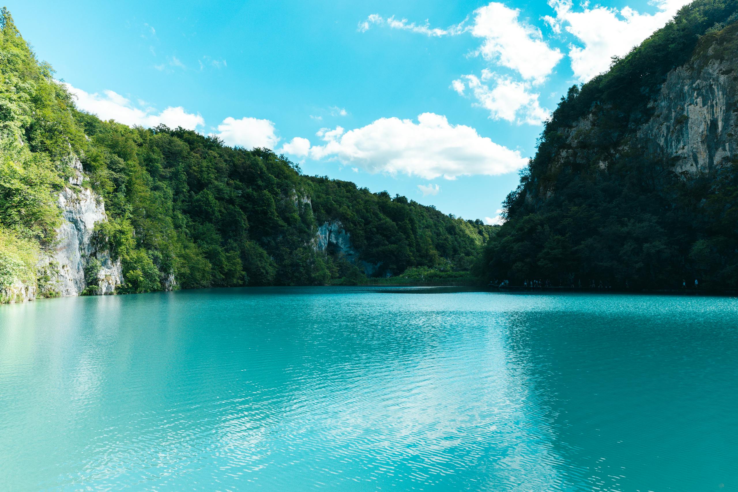 Explore the serene turquoise waters surrounded by lush greenery and cliffs in Plitvice Lakes National Park, Croatia.